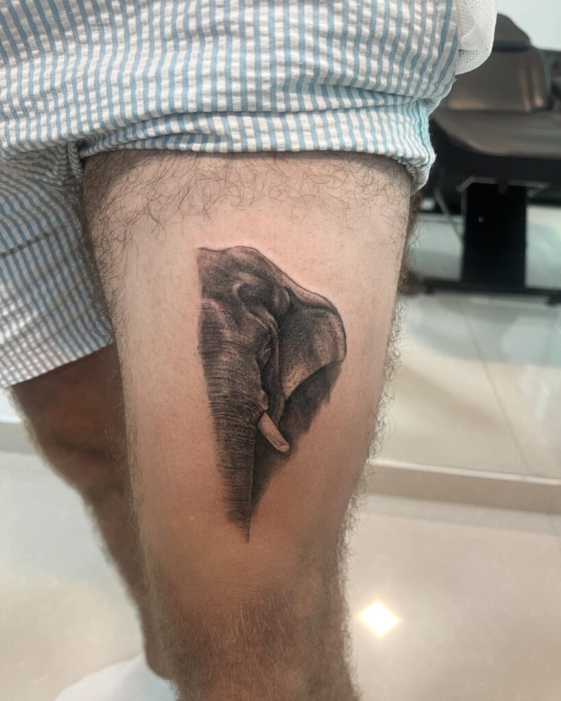 Half Asian elephant head tattoo on thigh for men, realistic black and grey rendering Asian majesty