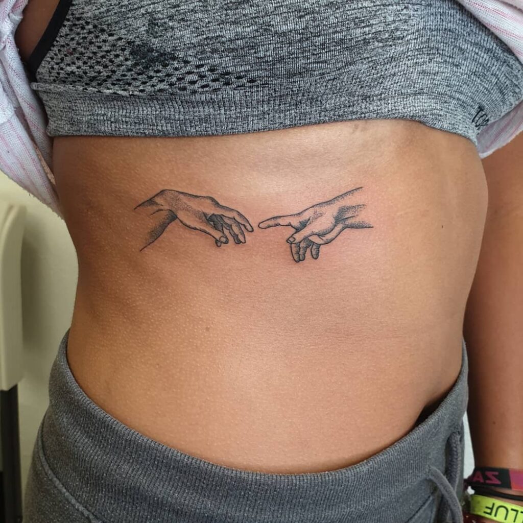 Hands from the creation of adam tattooed on rib classic art inspired ink