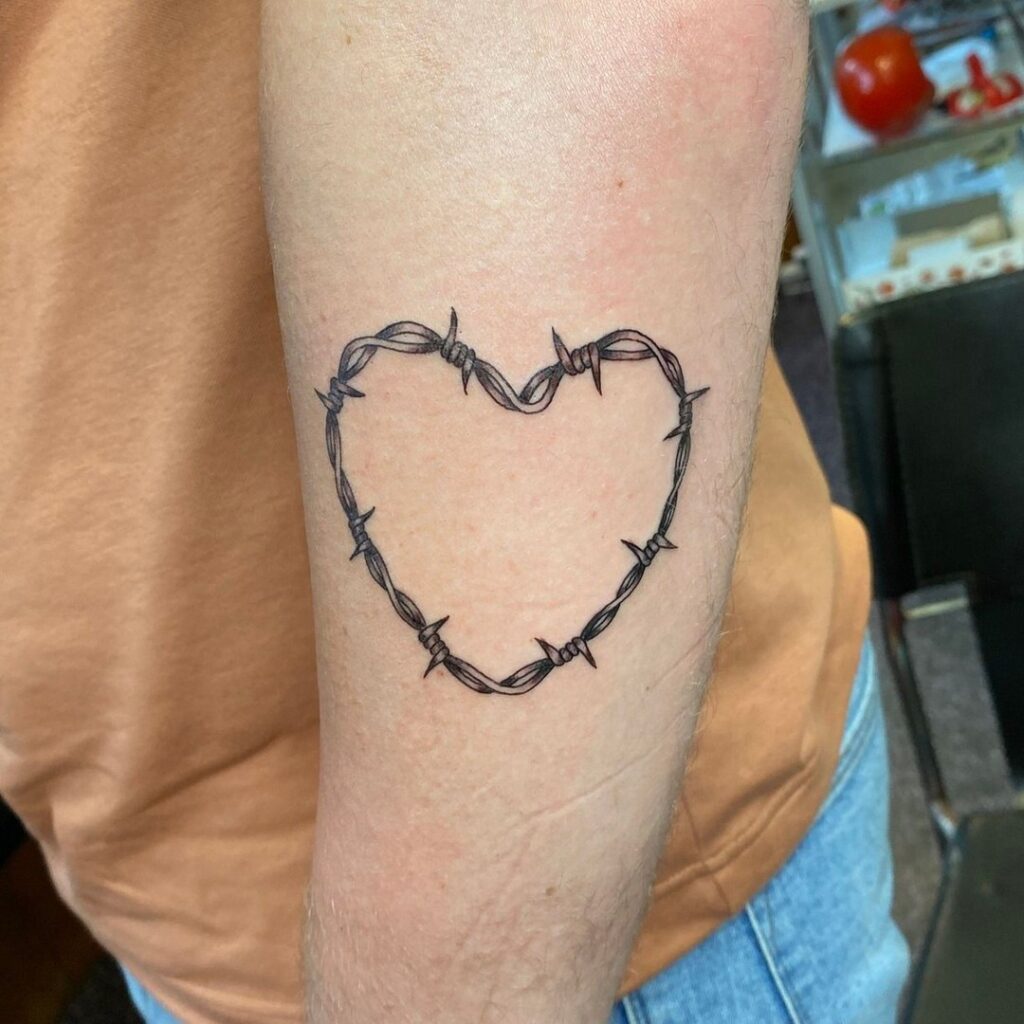 Heart outline shape surrounded by barbed wire on outer forearm symbolic body art