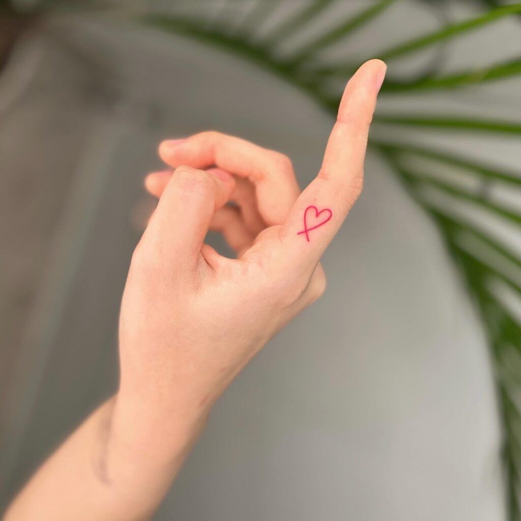 Heart tattoo on the side of the forefinger, red outline with intricate lines intersecting heartstrings