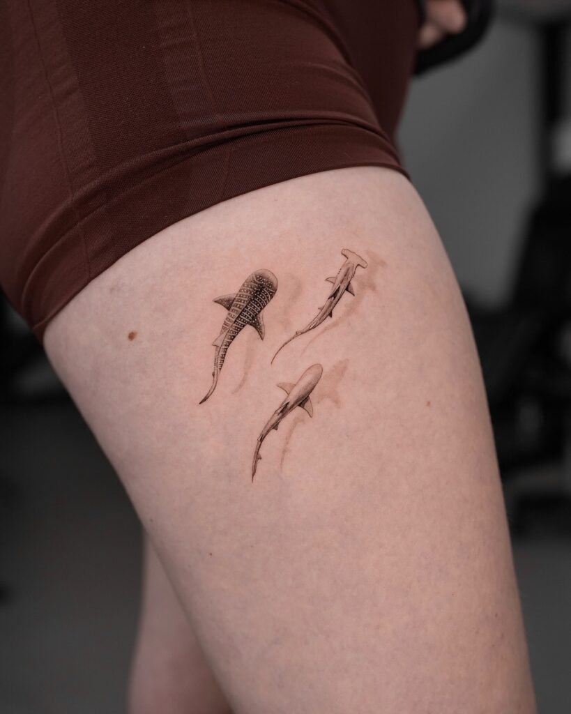 Highly detailed realistic three-shark tattoo on upper thigh symbolizing strength and resilience