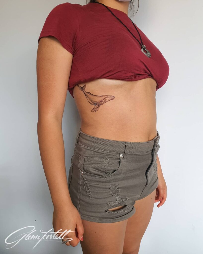 Humpback whale tattoo on the rib for girls, black and grey shaded, capturing the side view: majestic cetacean