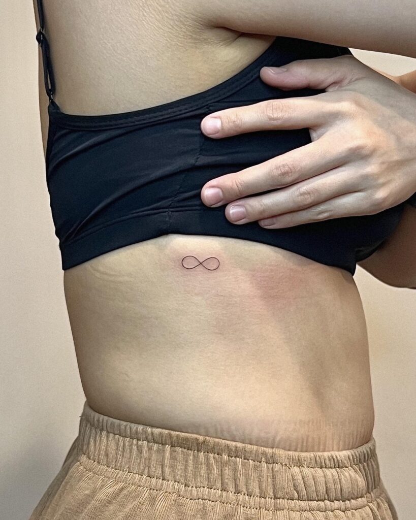 Infinity symbol fineline tattoo on the rib for females, a delicate and thin line: Endless elegance