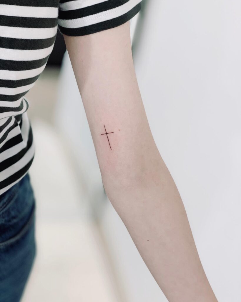 Inner elegance small cross tattoo above the elbow