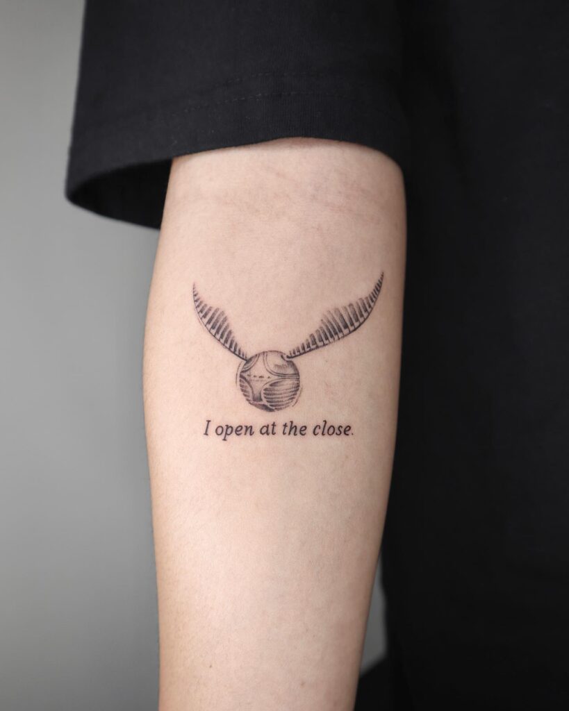 Inner forearm elegance golden snitch tattoo with 'I open at the close' lettering