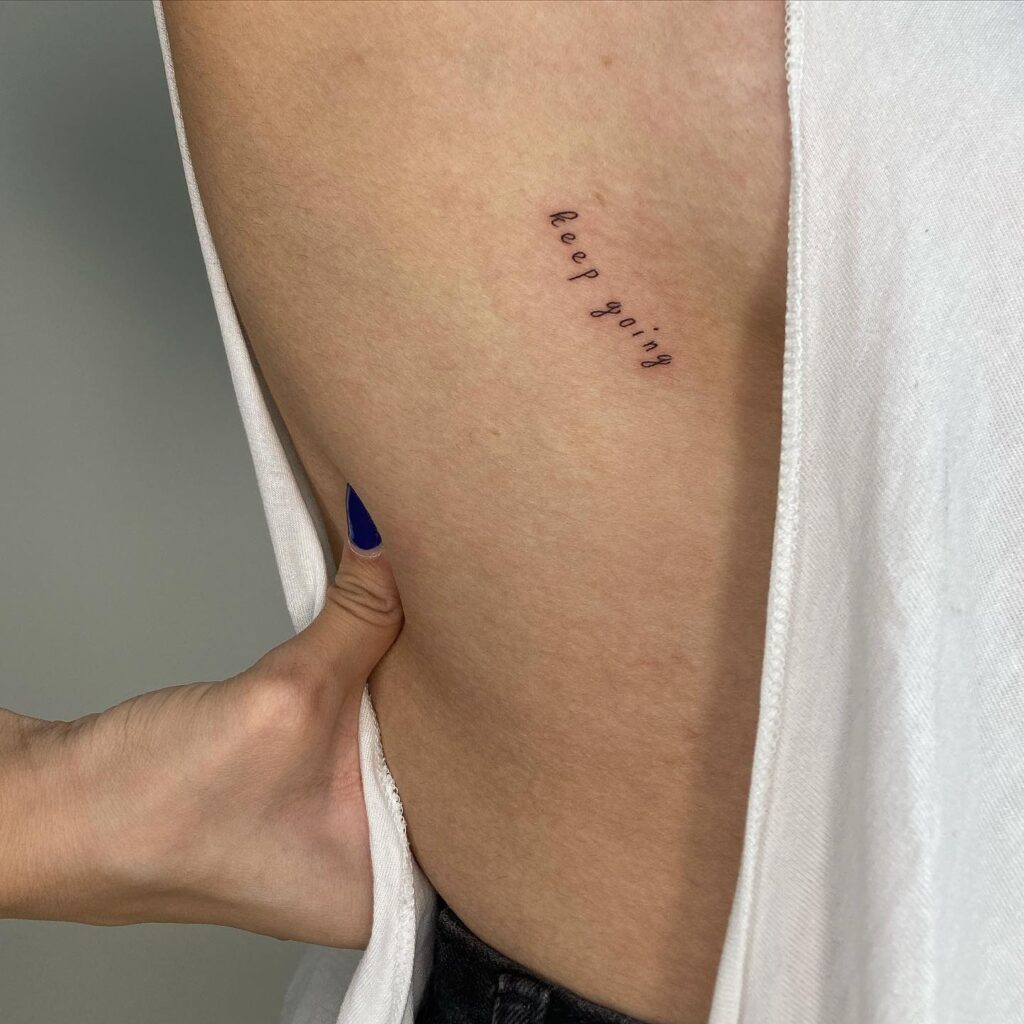 'Keep going' word tattoo on the rib, a tiny text reminder persistence whisper