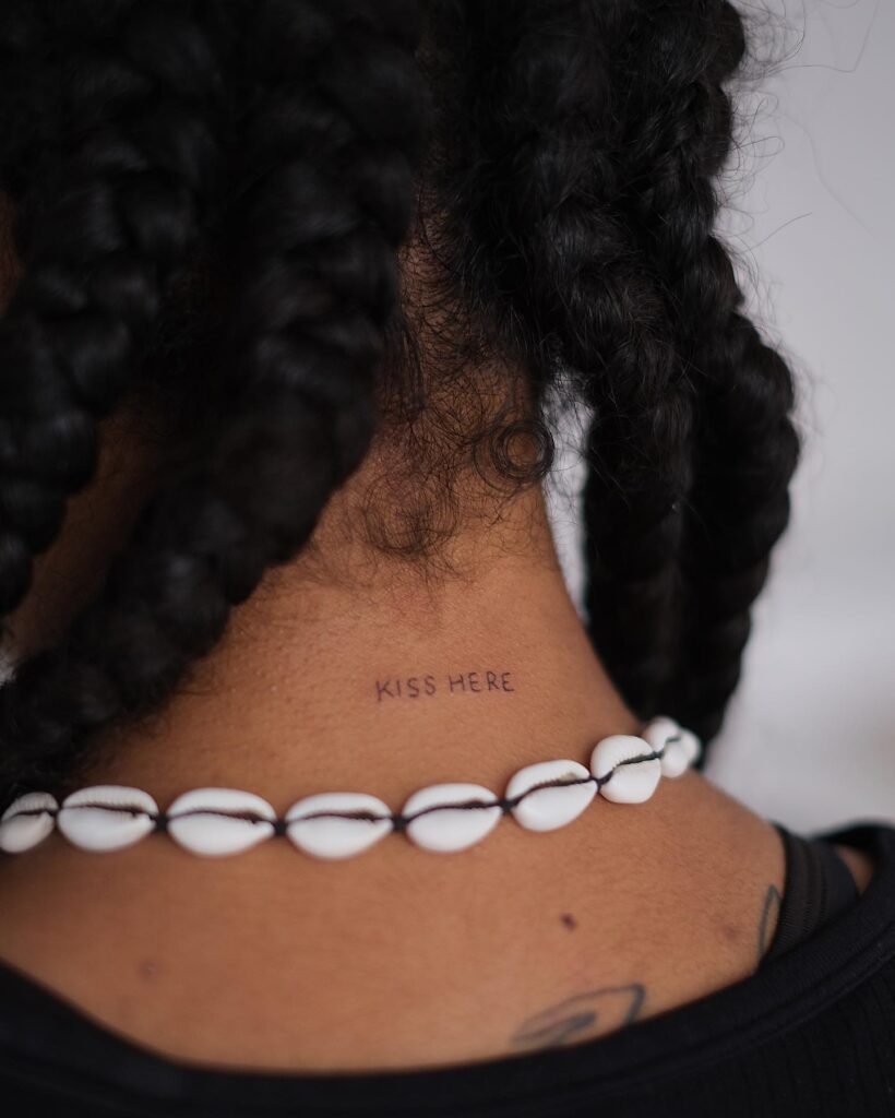 Kiss here tattoo on the back of the neck in small cursive font