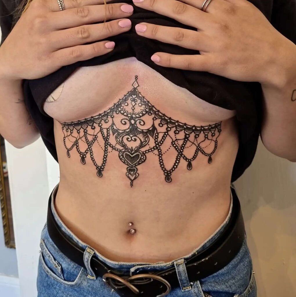 Lace-inspired ornamental sternum tattoo resembling jewelry or chandelier