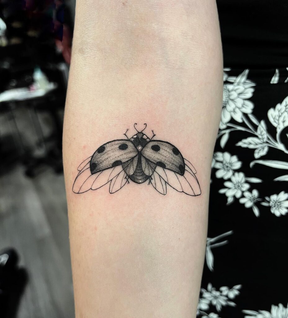 Ladybug tattoo on the forearm for females, black and grey shaded for a detailed look: luck in small things