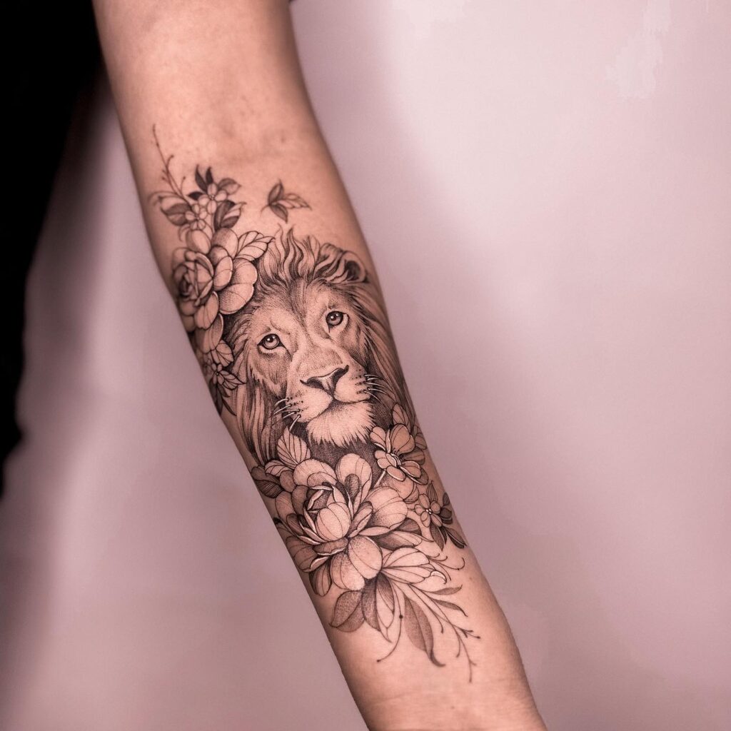 Lion head surrounded by florals on the forearm, darkly shaded for a striking and elegant tattoo floral sovereignty