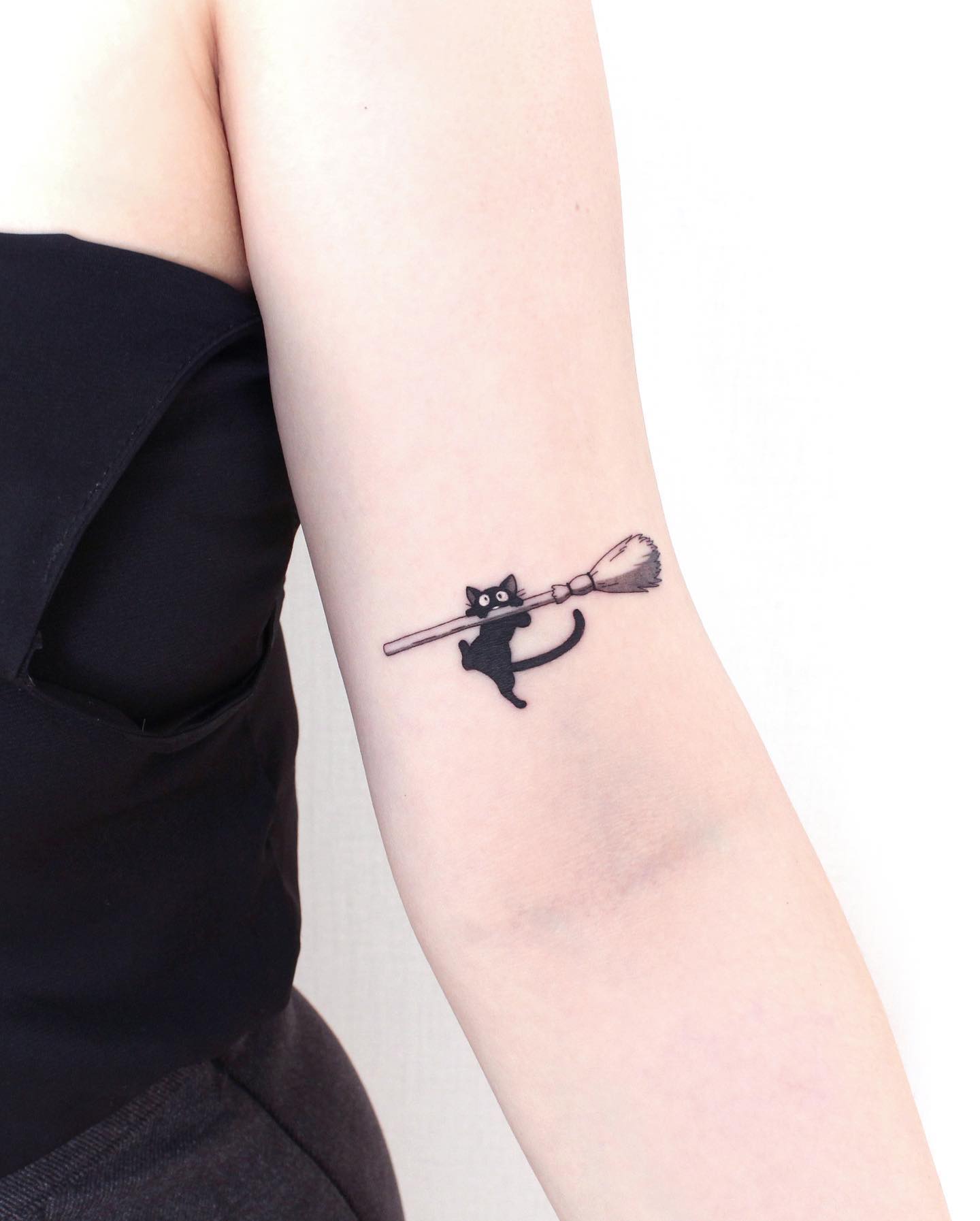 Magical black cat tattoo holding a broomstick, designed in a minimalist style, inspired by witchcraft and fantasy elements like Kiki’s Delivery Service