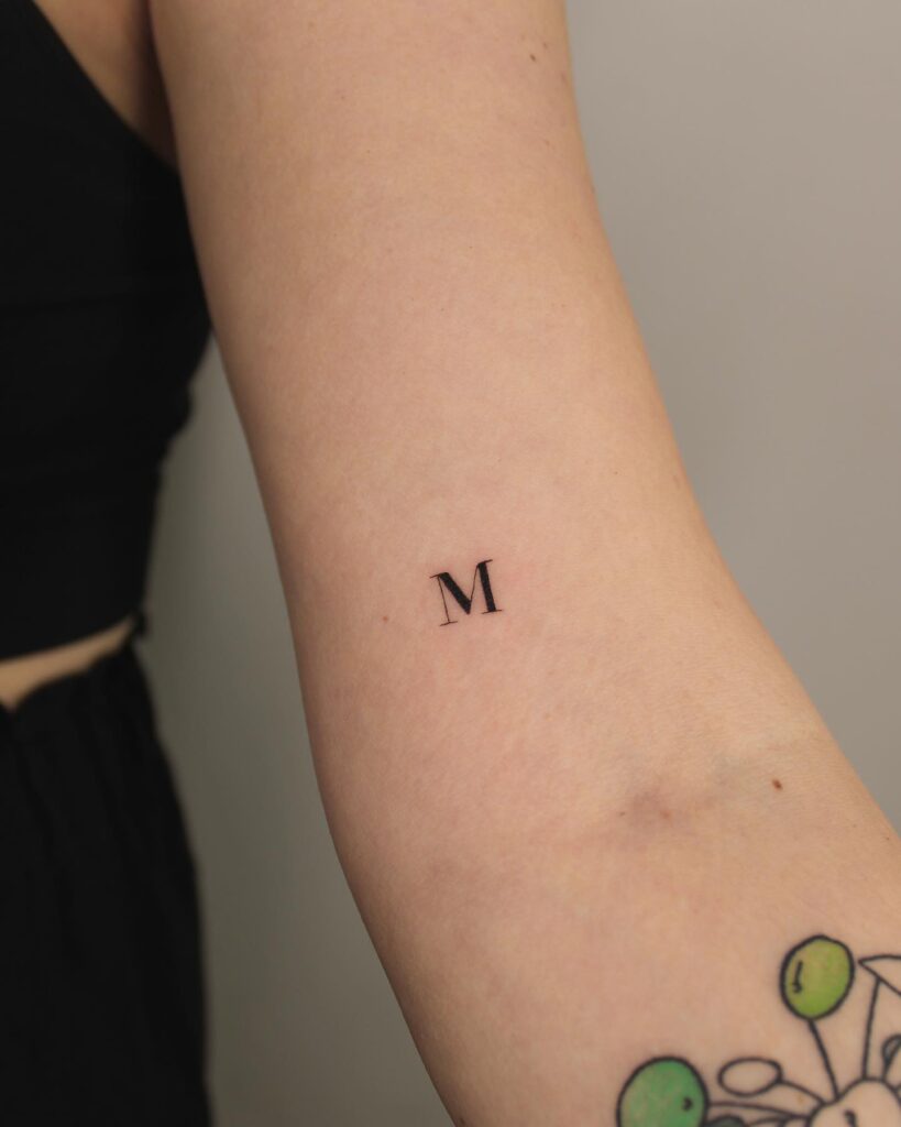 Majestic m elegant m letter tattoo above the elbow
