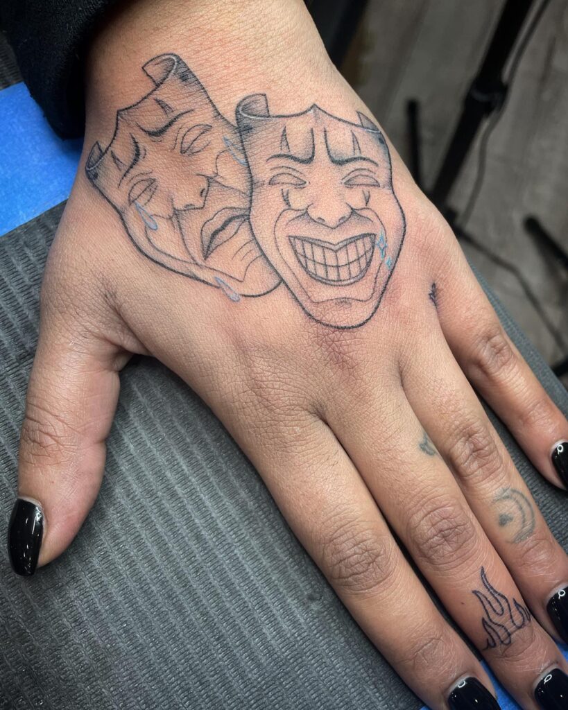 Masked emotions laugh now cry later hand tattoo 