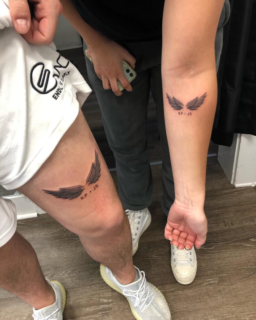 Matching Wings Tattoos with 'KP.JS' Lettering on Thigh and Forearm Couple Tattoo: Inked Bonds