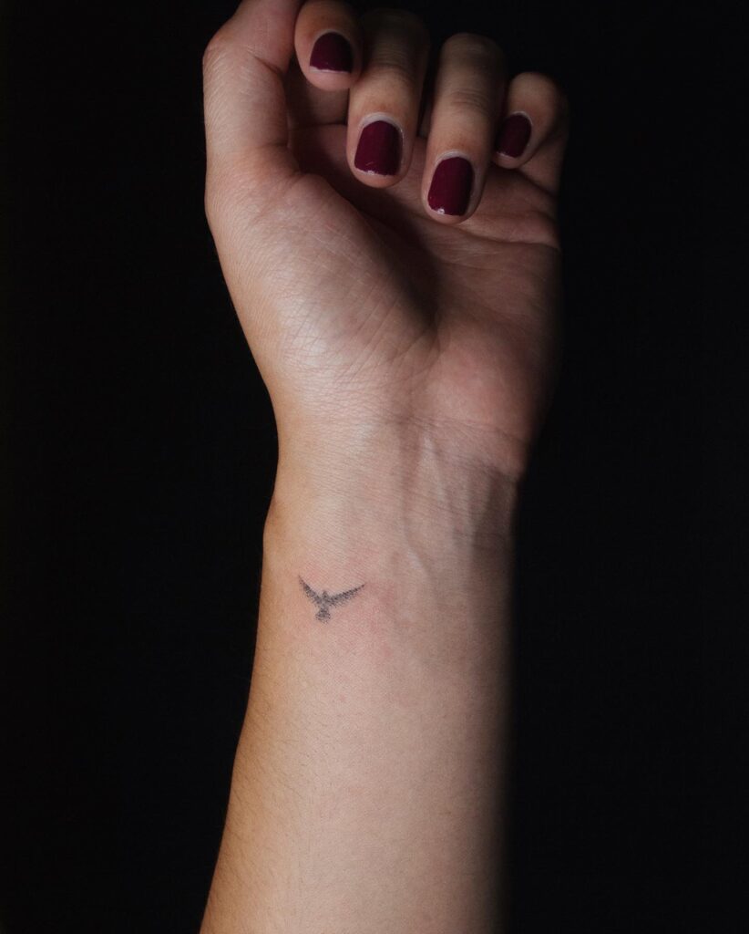 Micro Bird Inner Wrist Tattoo, a Very Small Grey Shaded Tattoo Capturing the Essence of Freedom: Featherlight Flight
