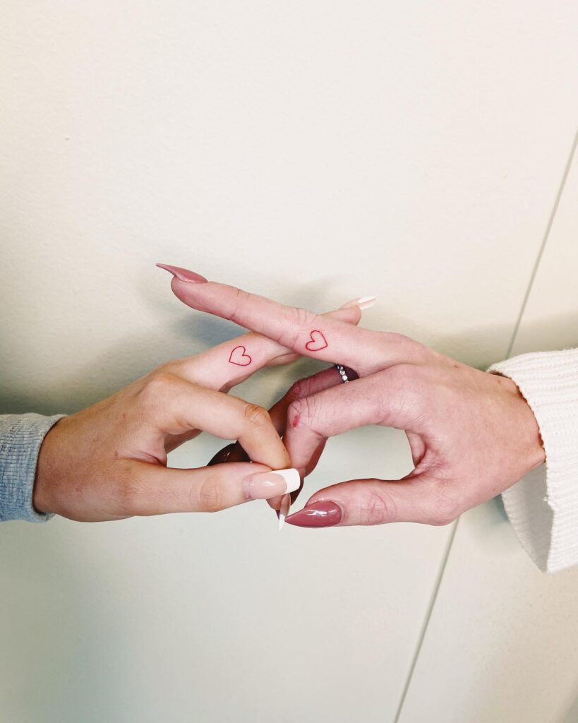 Middle finger side tattoo: red outline heart tattoo as a matching friendship tattoo