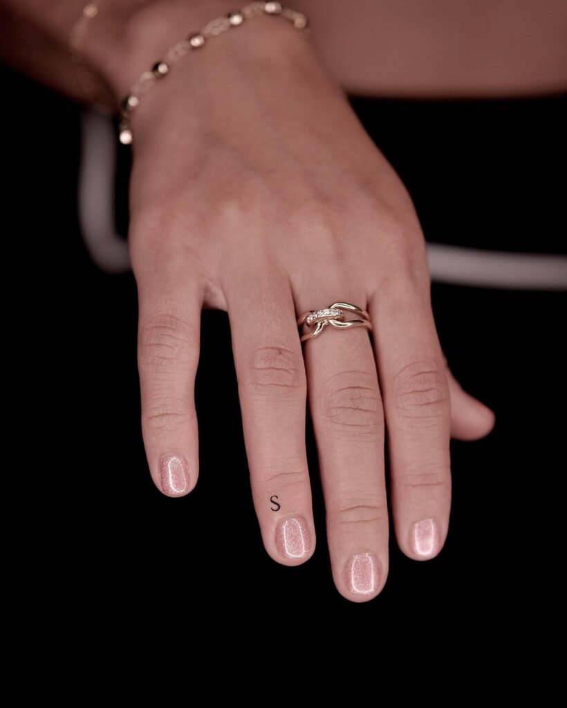 Miniature S Tattoo Near the Nail of the Ring Finger Blackwork Style for Understated Glamour Subtle S