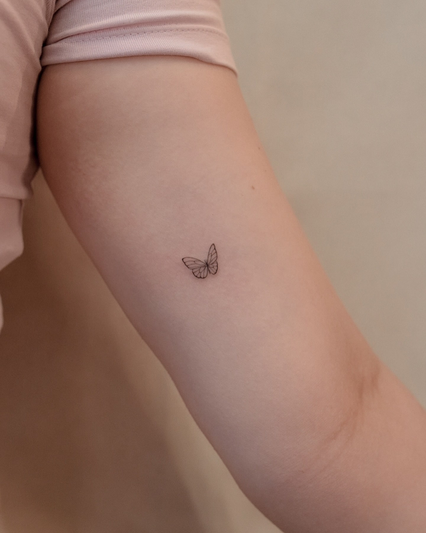 Minimal inner arm butterfly tattoo with fine line design near elbow