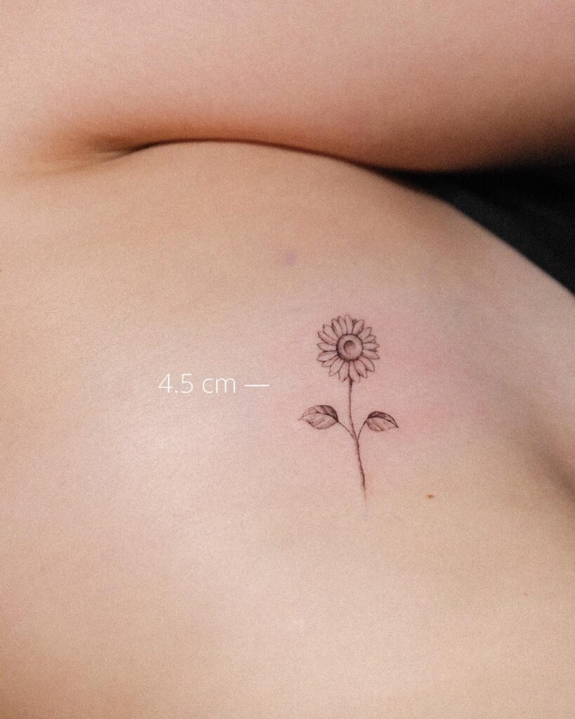 Minimal realistic sunflower tattoo on the rib: sunlit petals