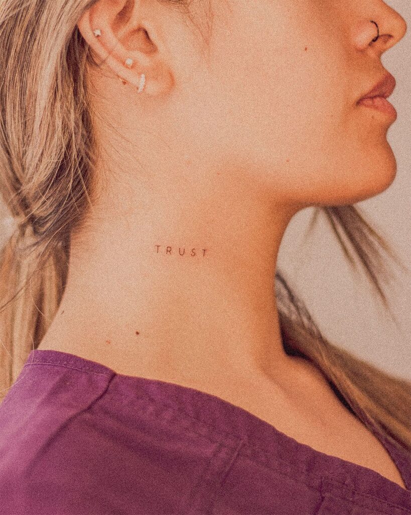 Minimal 'trust' word lettering tattoo on the side of the neck for a subtle reminder core value ink
