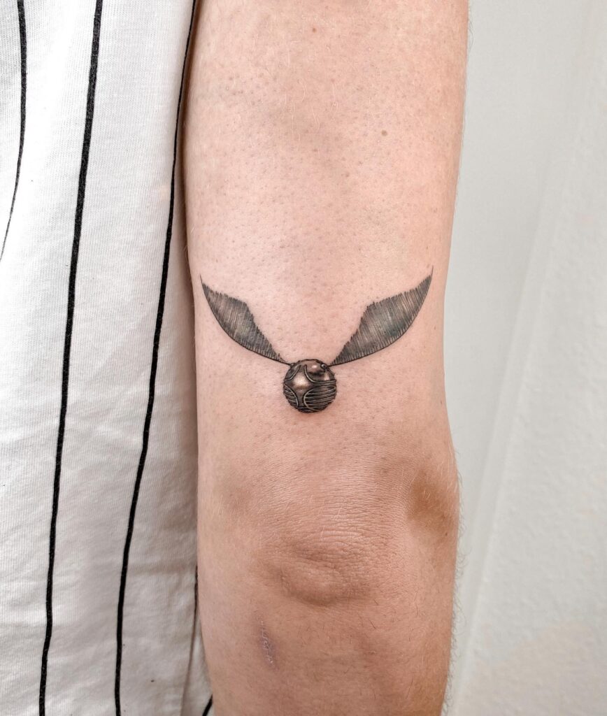 Minimalist back under elbow golden snitch tattoo subtle elegance