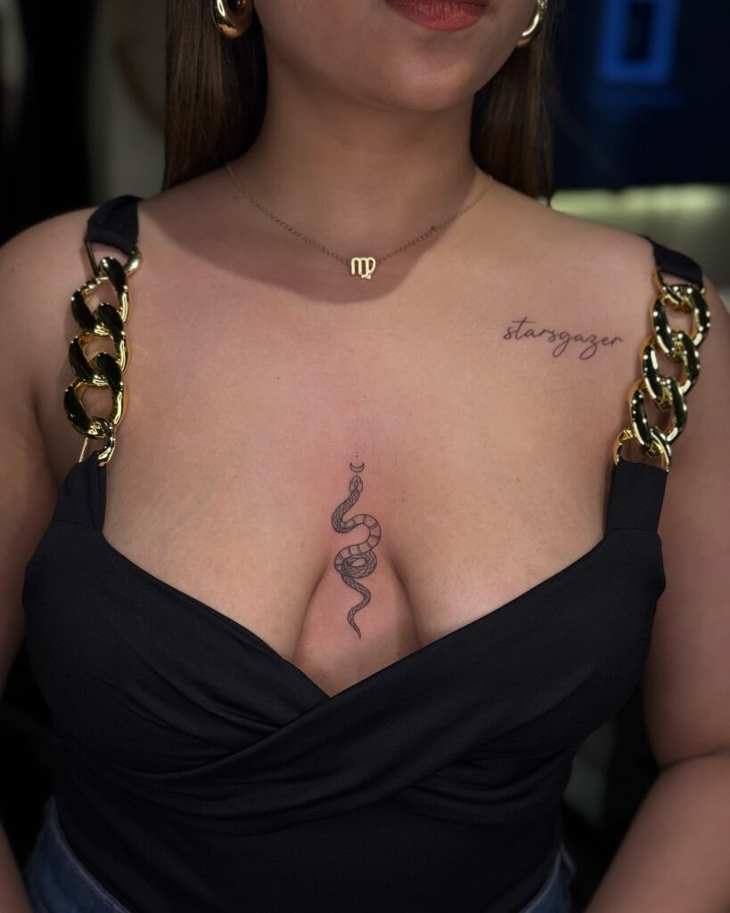 Minimalist coiled snake sternum tattoo with crescent moon symbolism