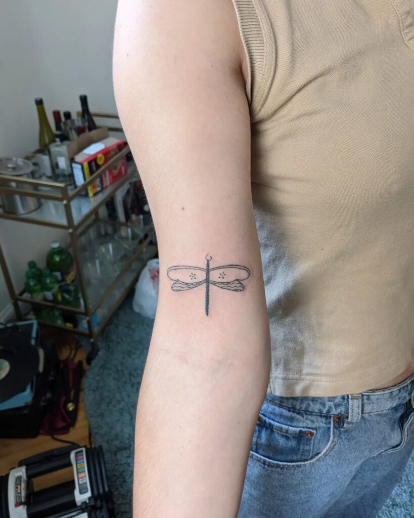 Minimalist Dragonfly Tattoo on Outer Arm Simple and Elegant Ink Idea