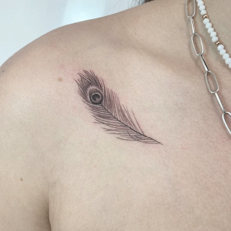 Minimalist elegance stylish peacock feather tattoo on a woman’s collarbone