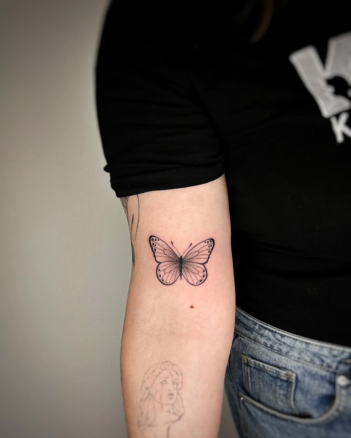 Minimalist fine line butterfly tattoo upper forearm with dotwork