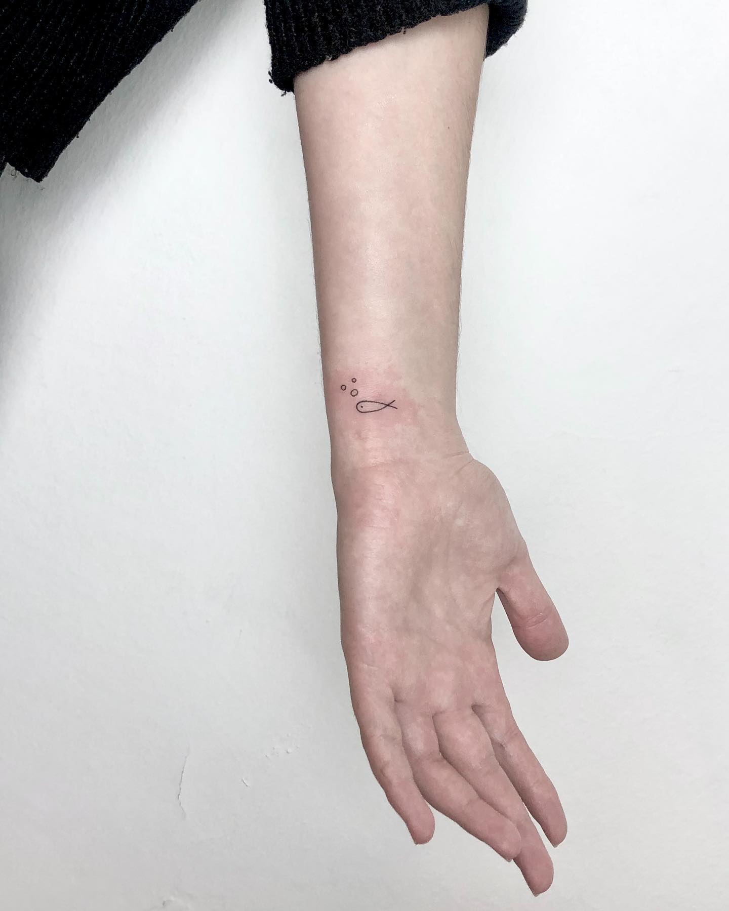 Minimalist Fish and Bubbles Wrist Tattoo Symbolizing Freedom and Nature
