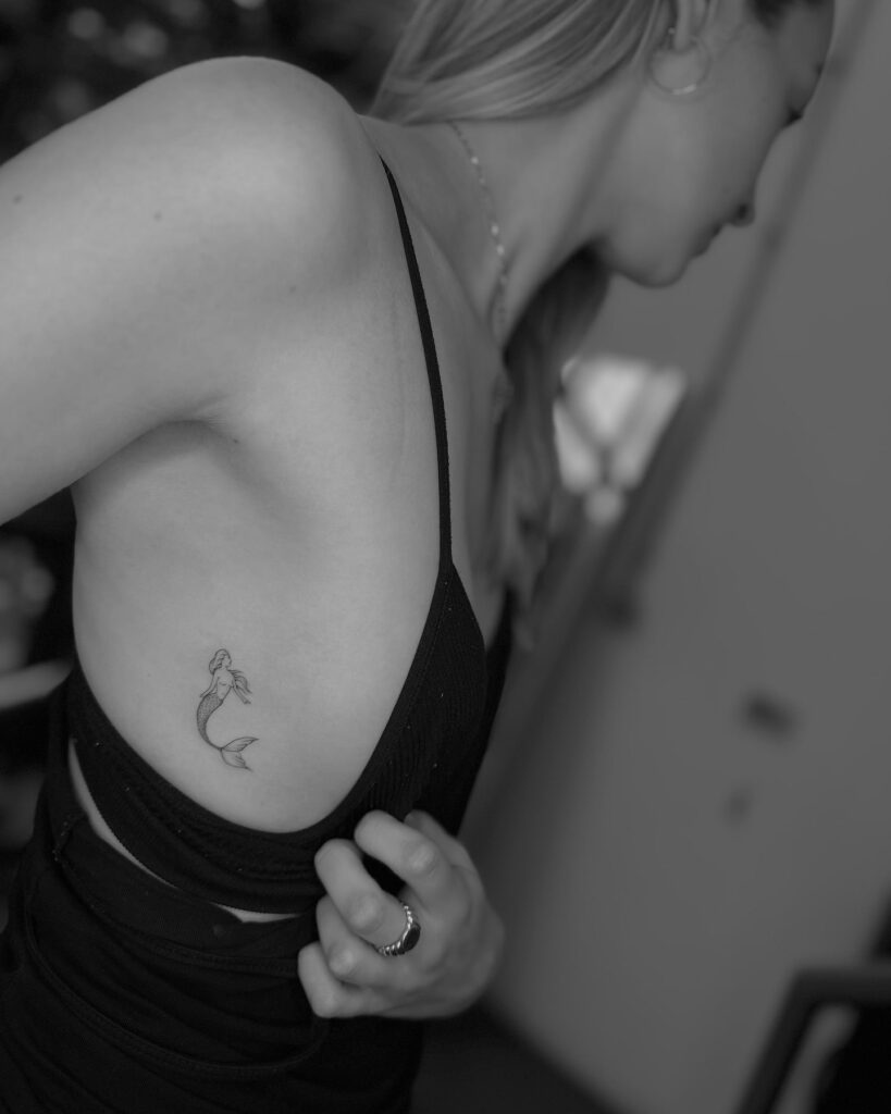Minimalist small mermaid tattoo on the rib: mermaid whispers
