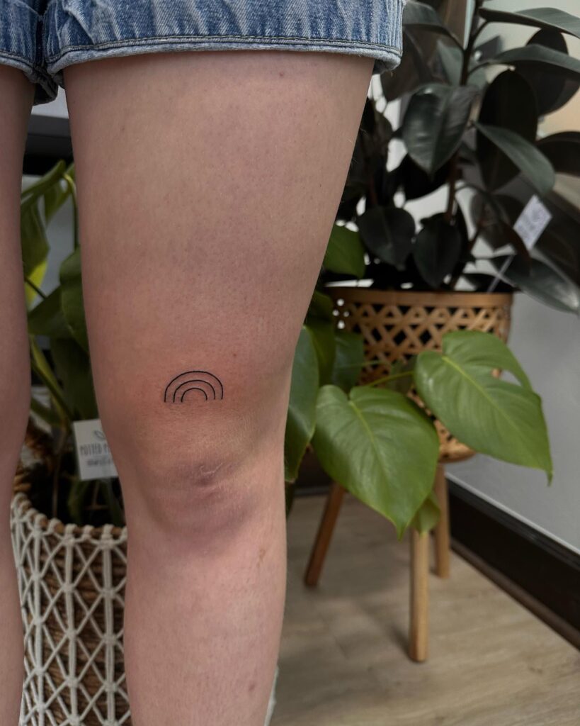 Minimalist small rainbow tattoo above the knee a delicate spectrum