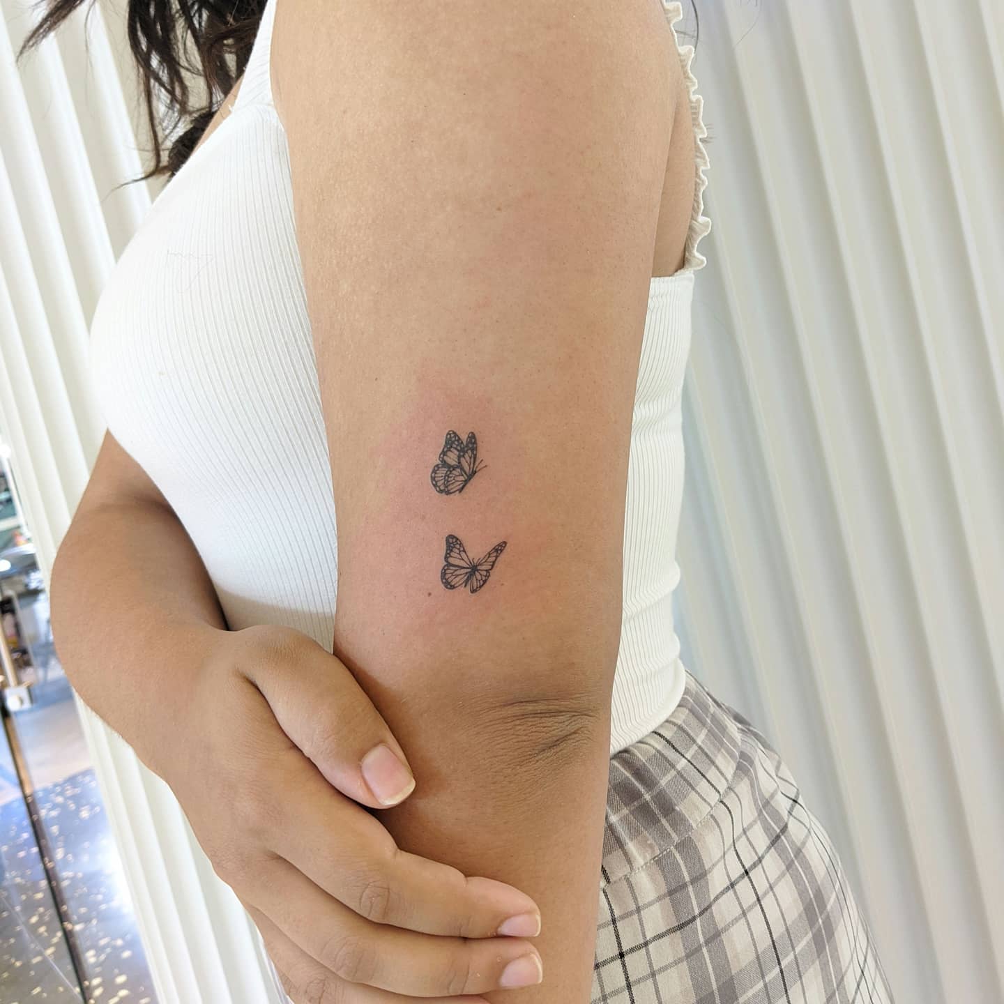 Minimalist upper arm back tattoo with two dainty butterflies in flight