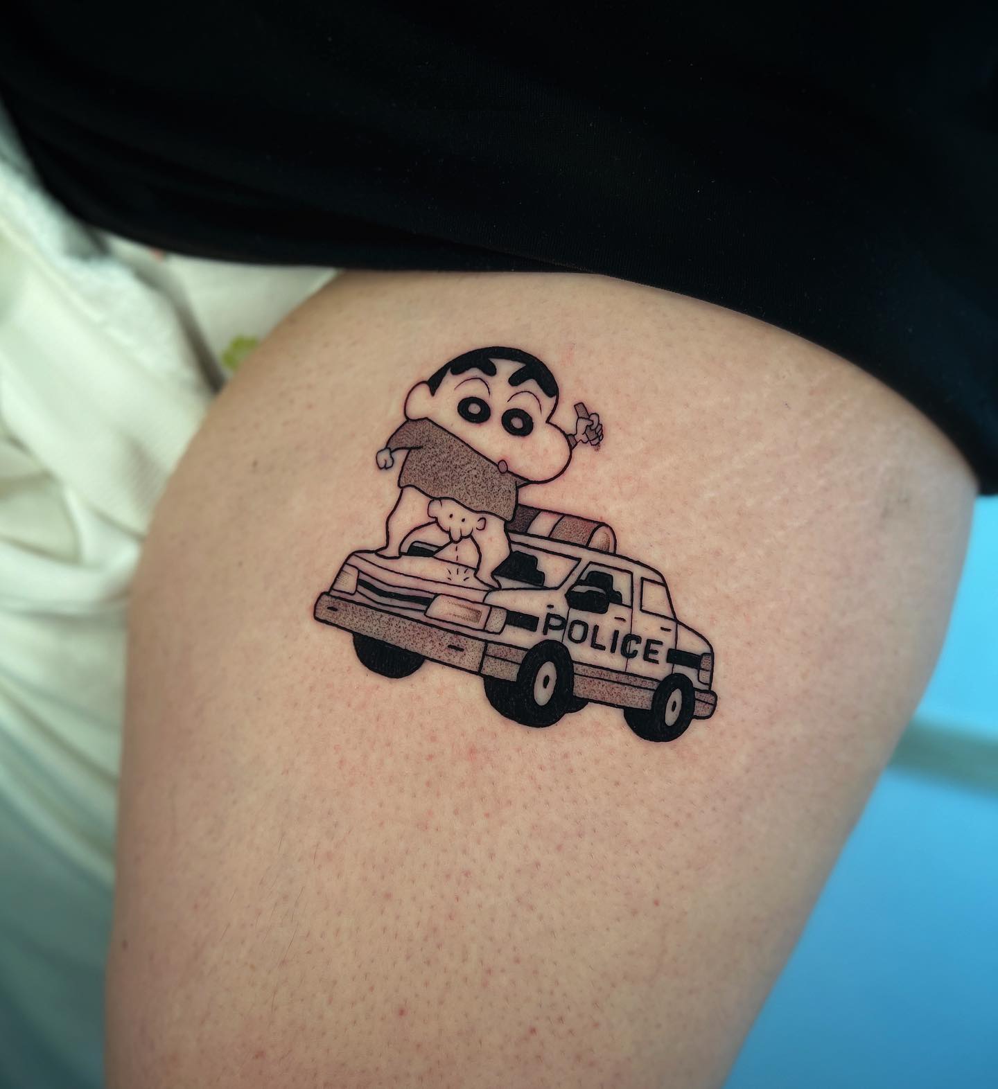Mischievous Shin Chan tattoo standing on a police car with his signature cheeky pose, representing humor, defiance, and love for nostalgic Japanese anime