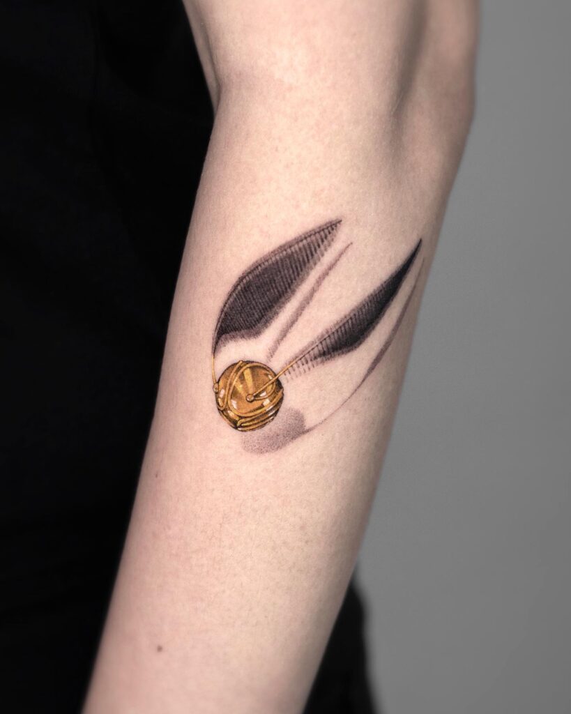 Near elbow 3d small golden snitch tattoo whimsical artistry