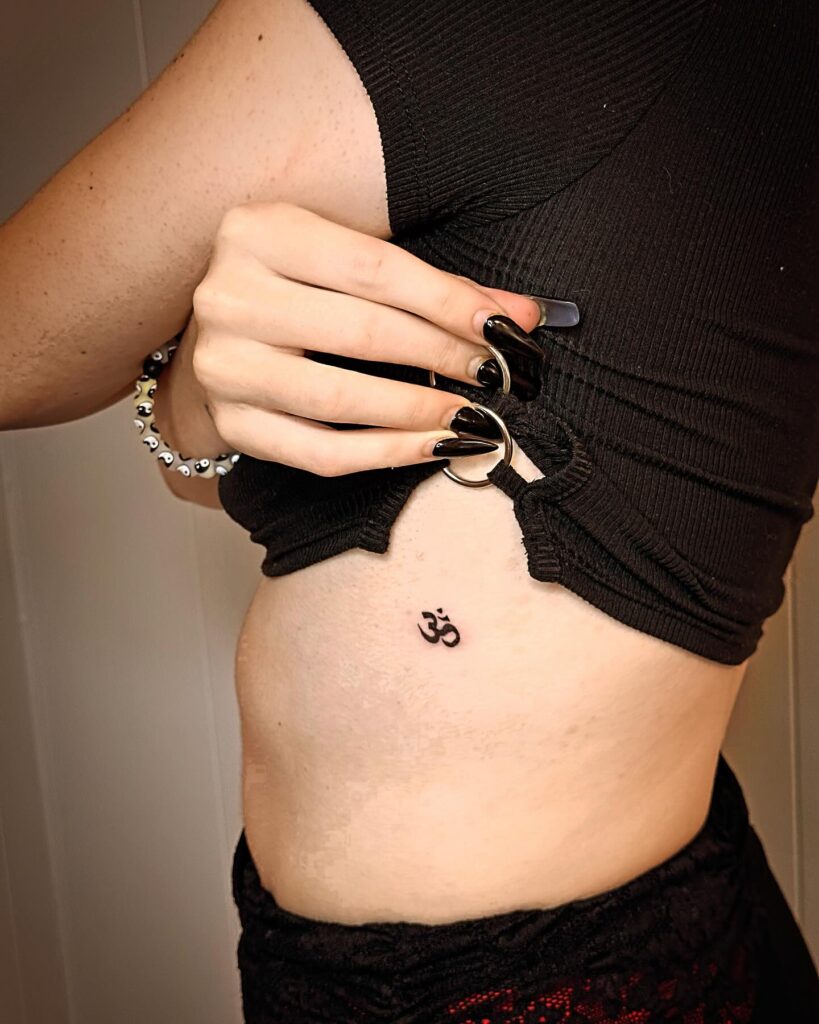 Om symbol tattoo on the rib with meticulous black ink work sacred symbolism