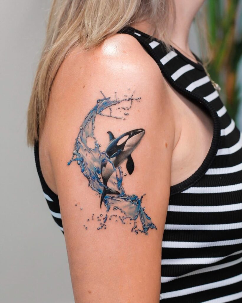 Orca tattoo with water splash effect and realistic shading on upper arm
