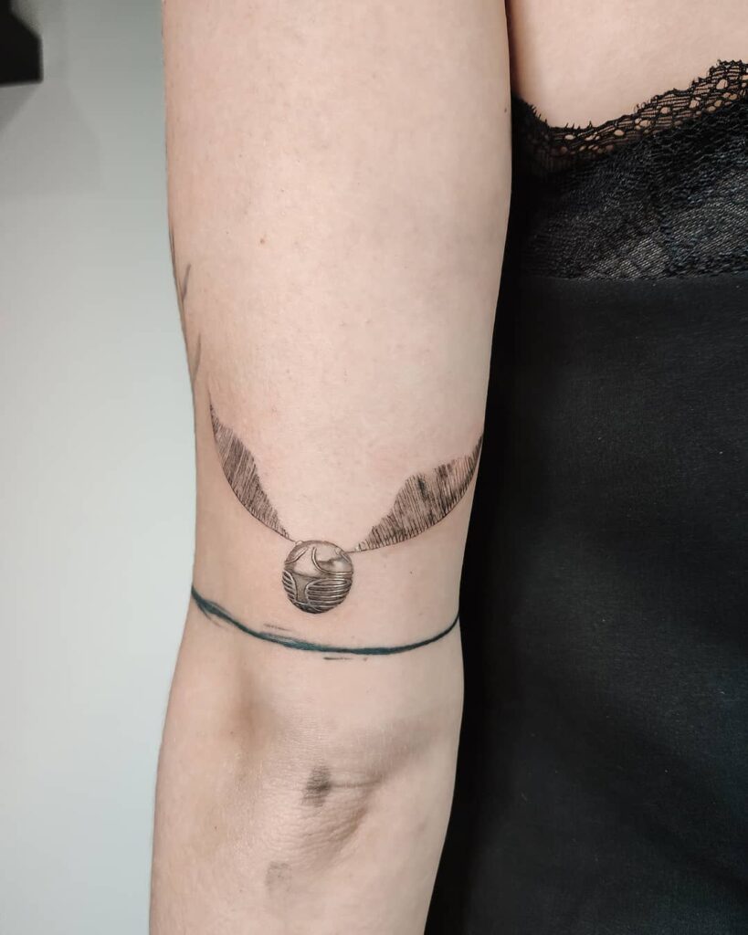 Outer arm enchantment golden snitch tattoo above the elbow