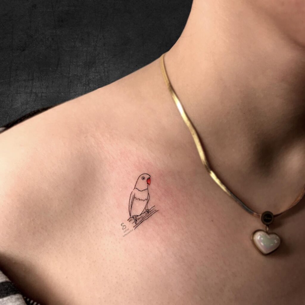 Parrot perched on a small wooden structure tattoo on the collarbone, featuring red beak and fineline outline tropical charm