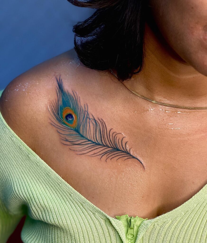Realism in color vibrant peacock feather tattoo on the collarbone for women