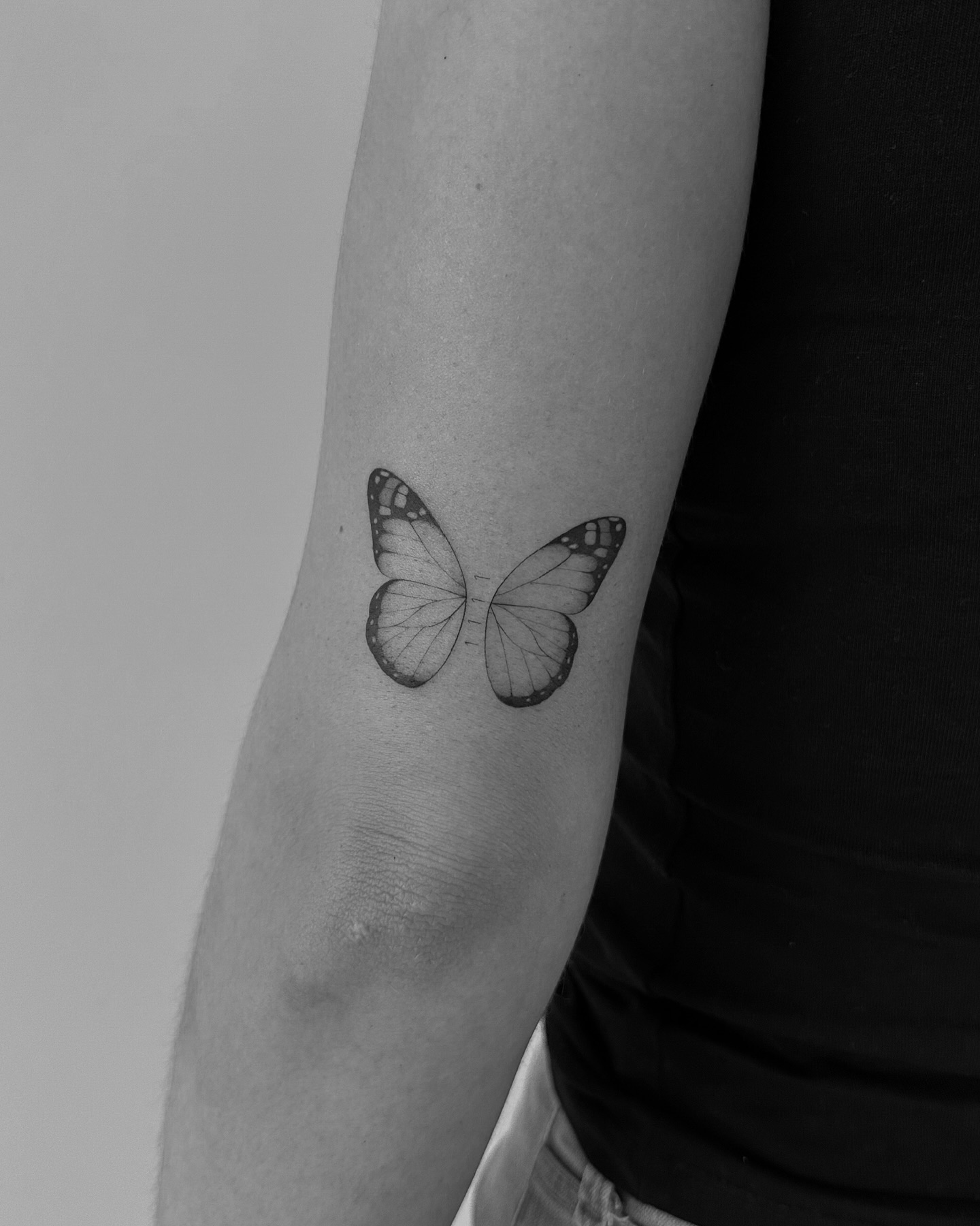 Realistic butterfly tattoo upper arm near elbow with soft gradients