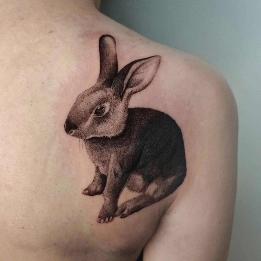 Realistic dark grey rabbit tattoo on the back of the shoulder for men
