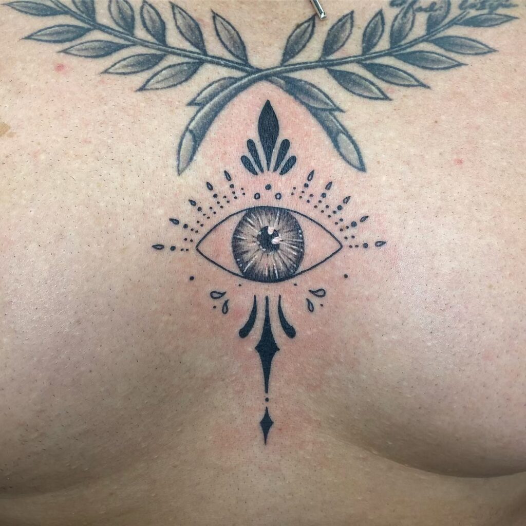 Realistic eye sternum tattoo with ornamental accents and spiritual symbolism