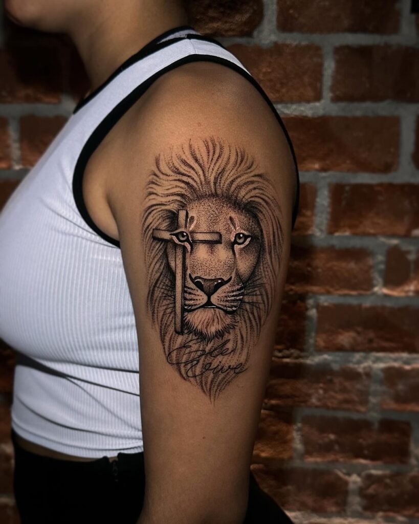 Realistic lion face tattoo on the upper arm with cross over the eye: intersection majesty