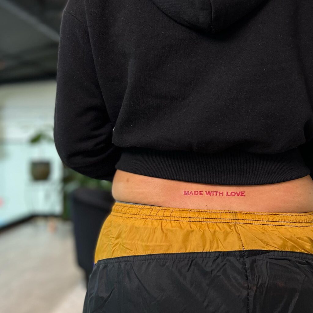 Red Text Lettering Tattoo on the Lower Back: Made with Love