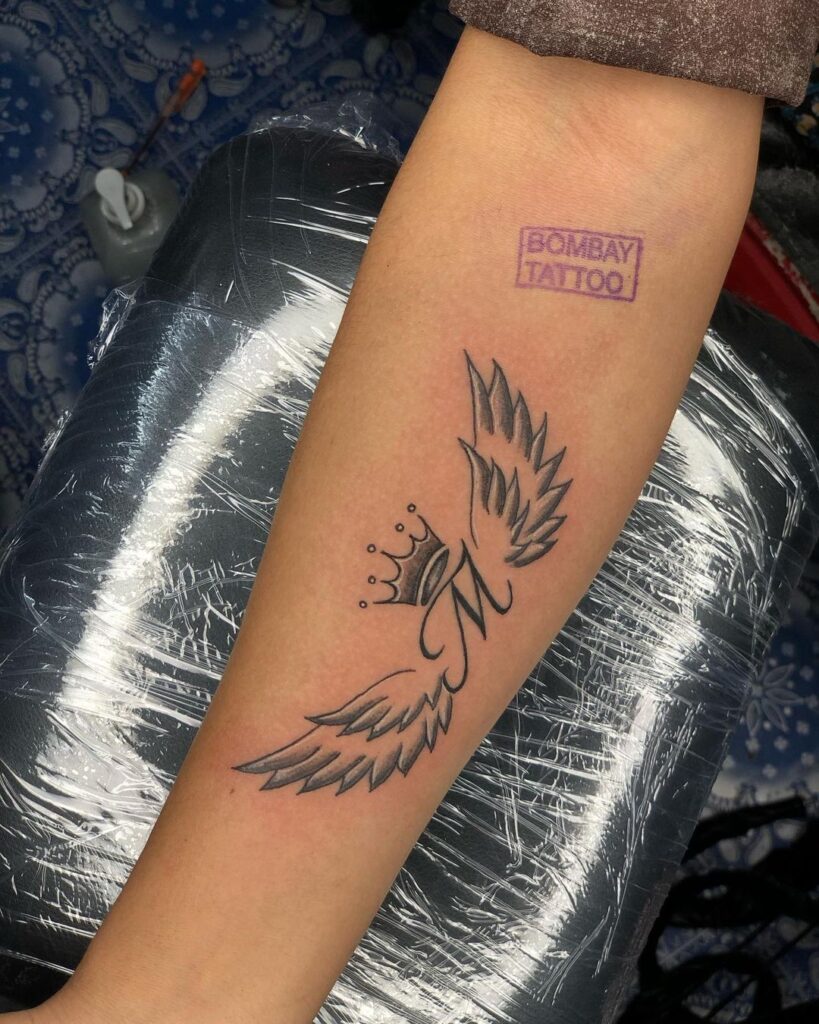 Regal statement m alphabet tattoo with wings & crown on the forearm