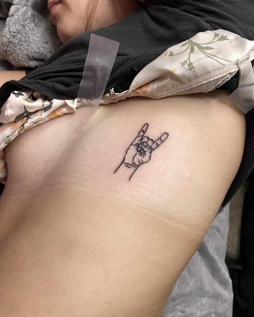 Rock hand tattoo on the side rib in black outline, a symbol of musical passion rock on
