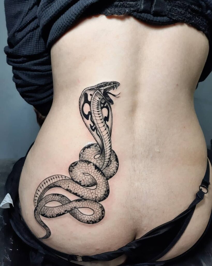 Side view cobra tattoo in black work on the lower back and hip, tongue out for extra charm: fierce femininity