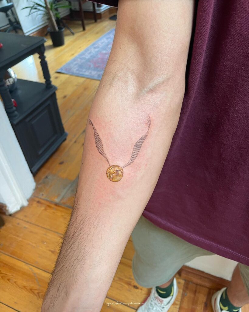 Simplicity meets enchantment simple golden snitch tattoo below the elbow