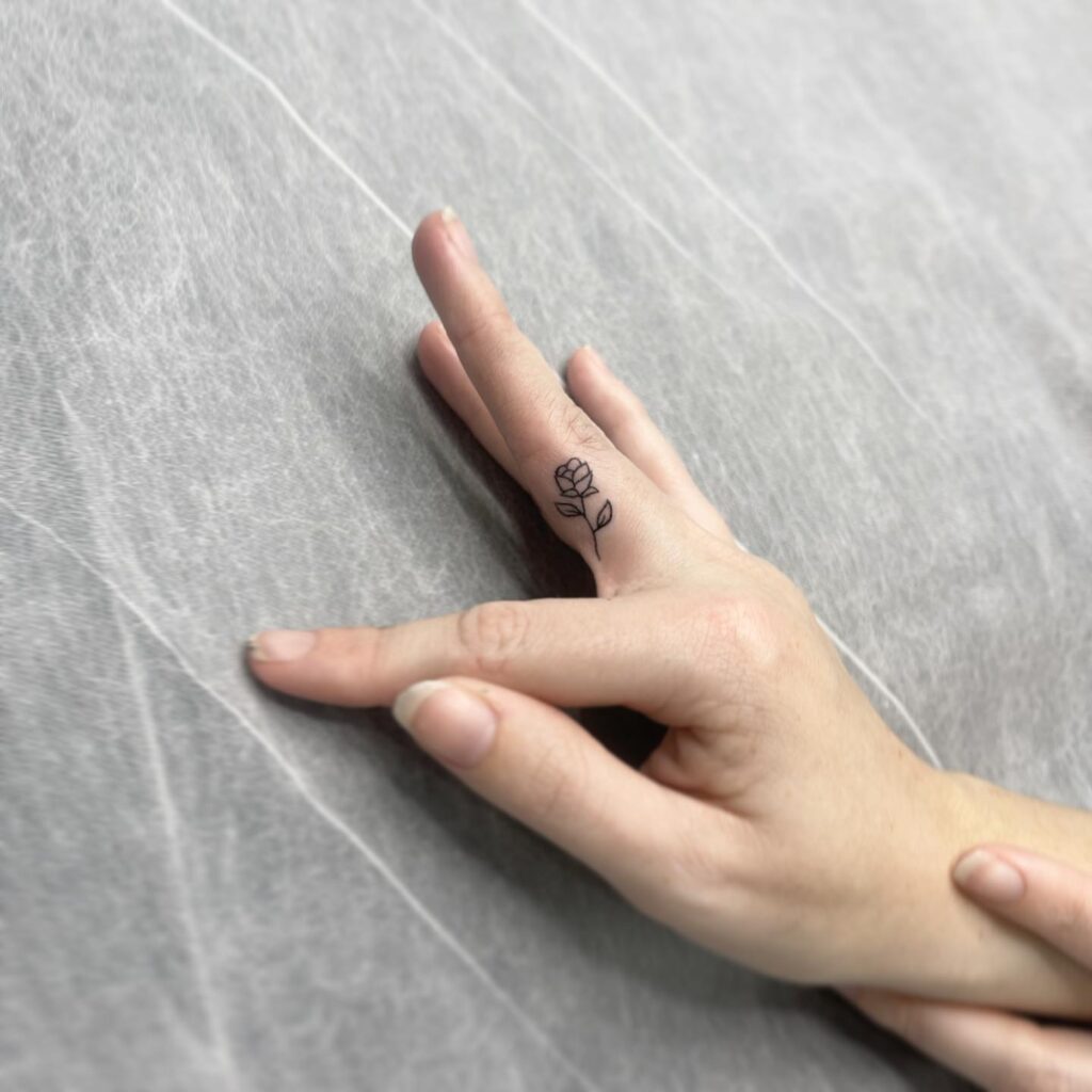 Small Rose Flower Plant Outline Tattoo on the Side of the Middle Finger Adding a Touch of Natures Elegance: Finger Bloom